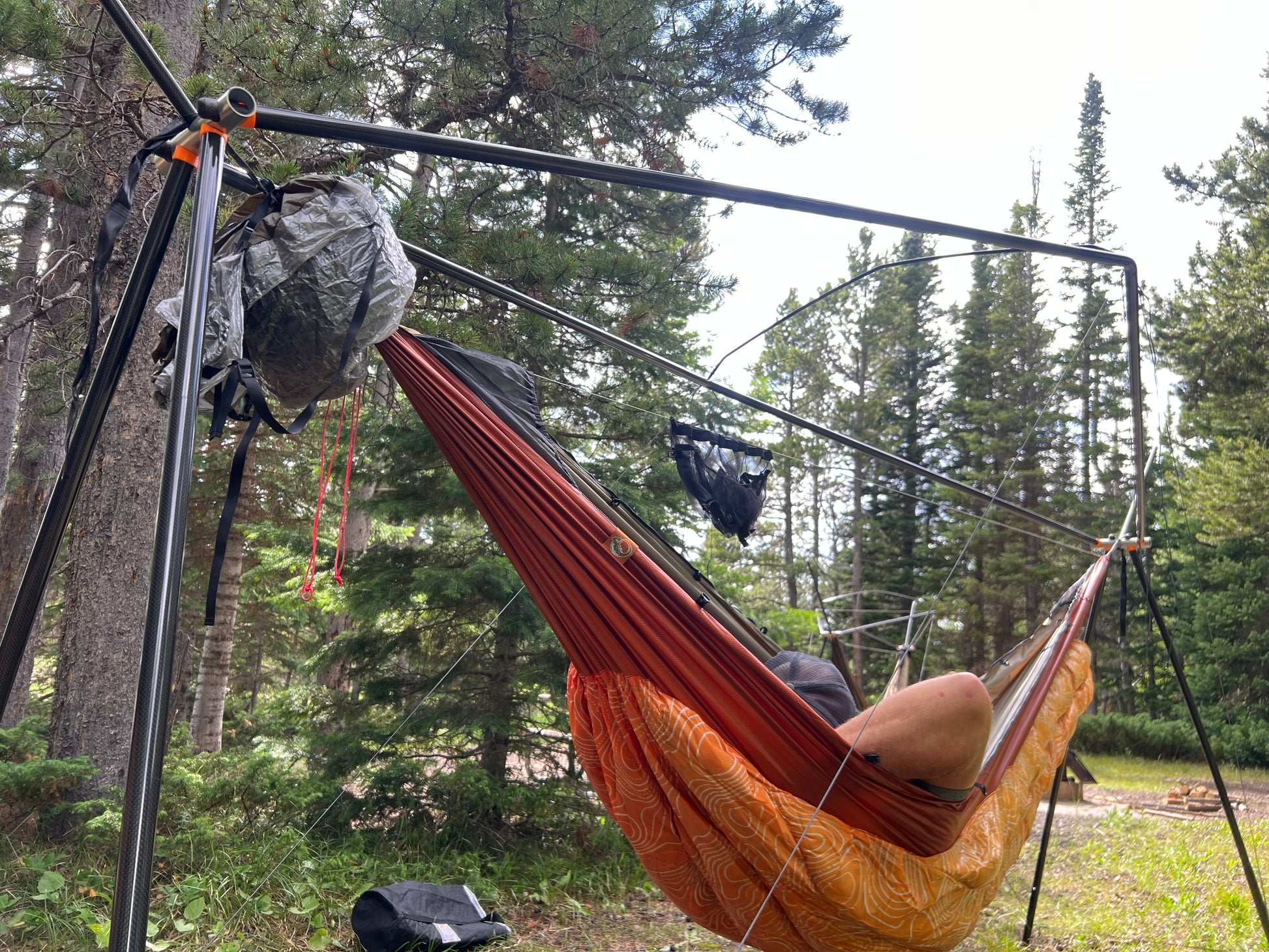 Person relaxing in a hammock on a cricket stand with camping gear in a forest setting