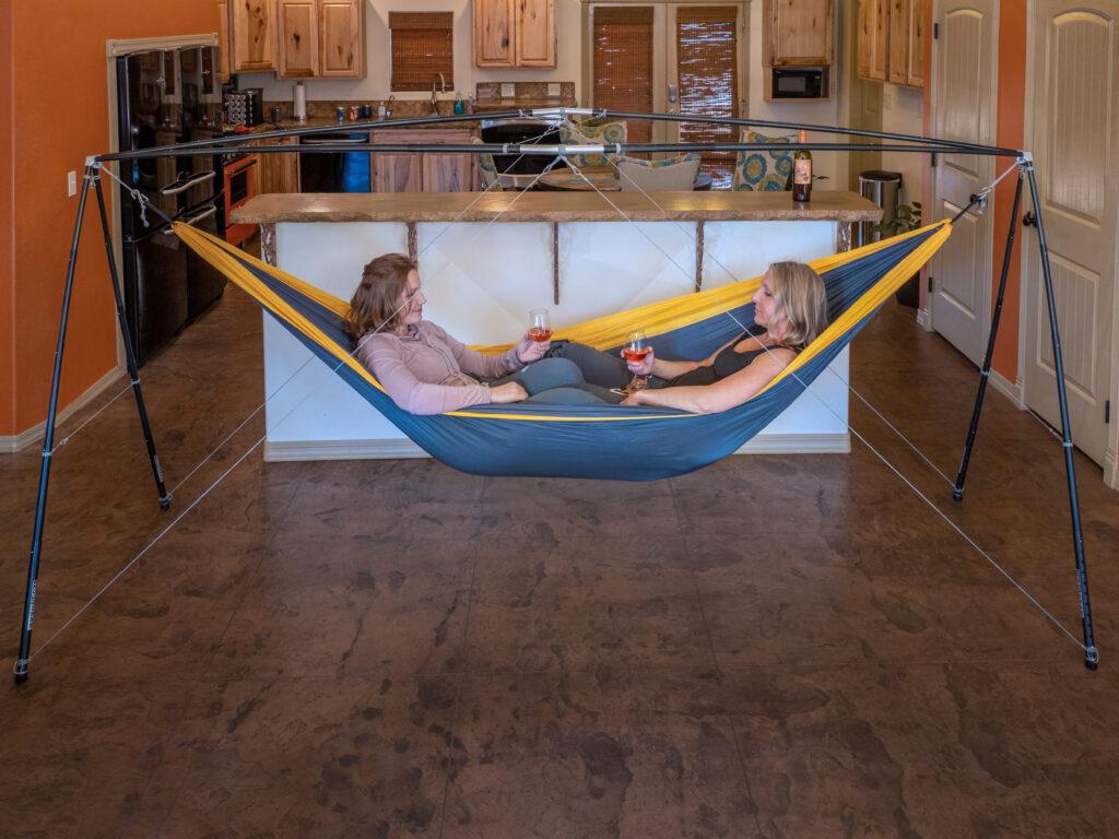 two women toasting wine indoors while sitting in a hammock stand